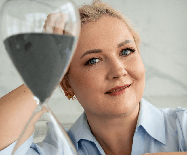 Simona Raganova šypsosi laikydama smėlio laikrodį, simbolizuojantį vidinės ramybės ir savęs pažinimo procesą